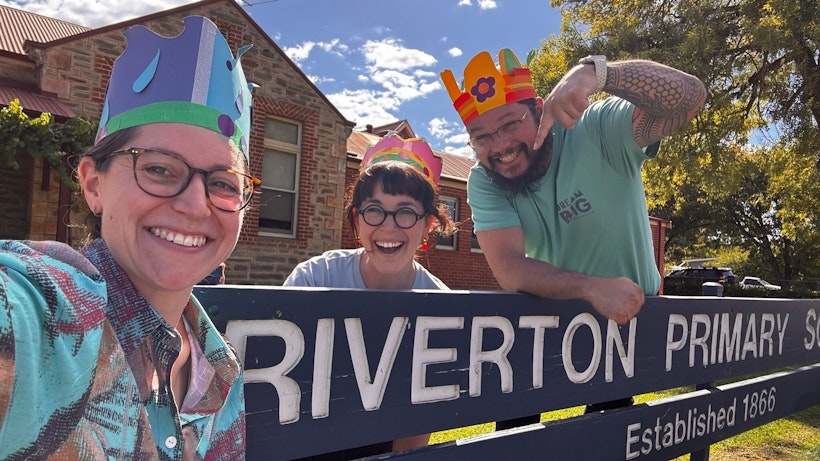 Two women and a man wearing cardboard birthday hats in front of a primary school